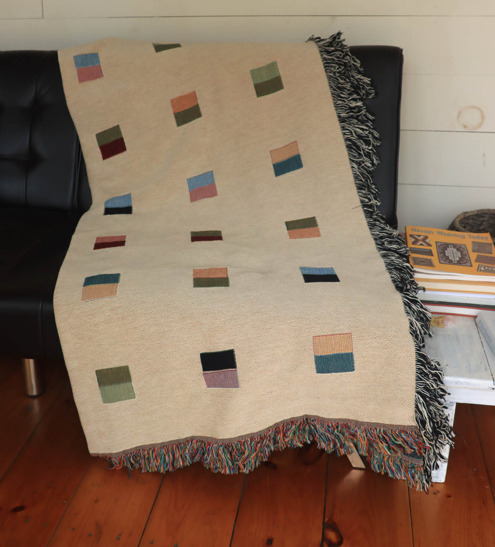 A cream-colored woven blanket with a Modern geometric split squares pattern of small multicolored squares and fringe edges. Scandinavian Design style for contemporary home decor.