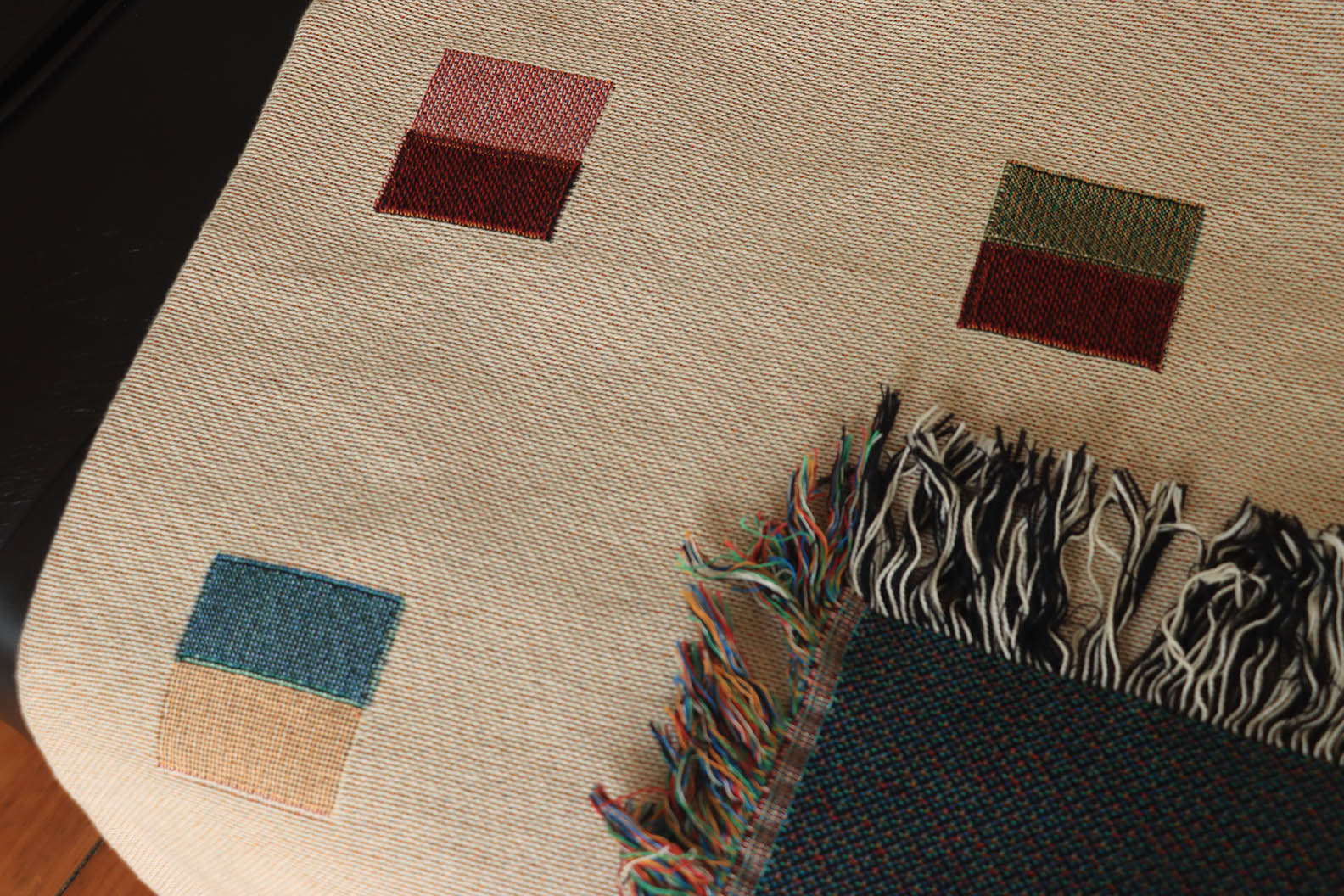 A cream-colored woven blanket with a Modern geometric split squares pattern of small multicolored squares and fringe edges. Scandinavia Design style for contemporary home decor.