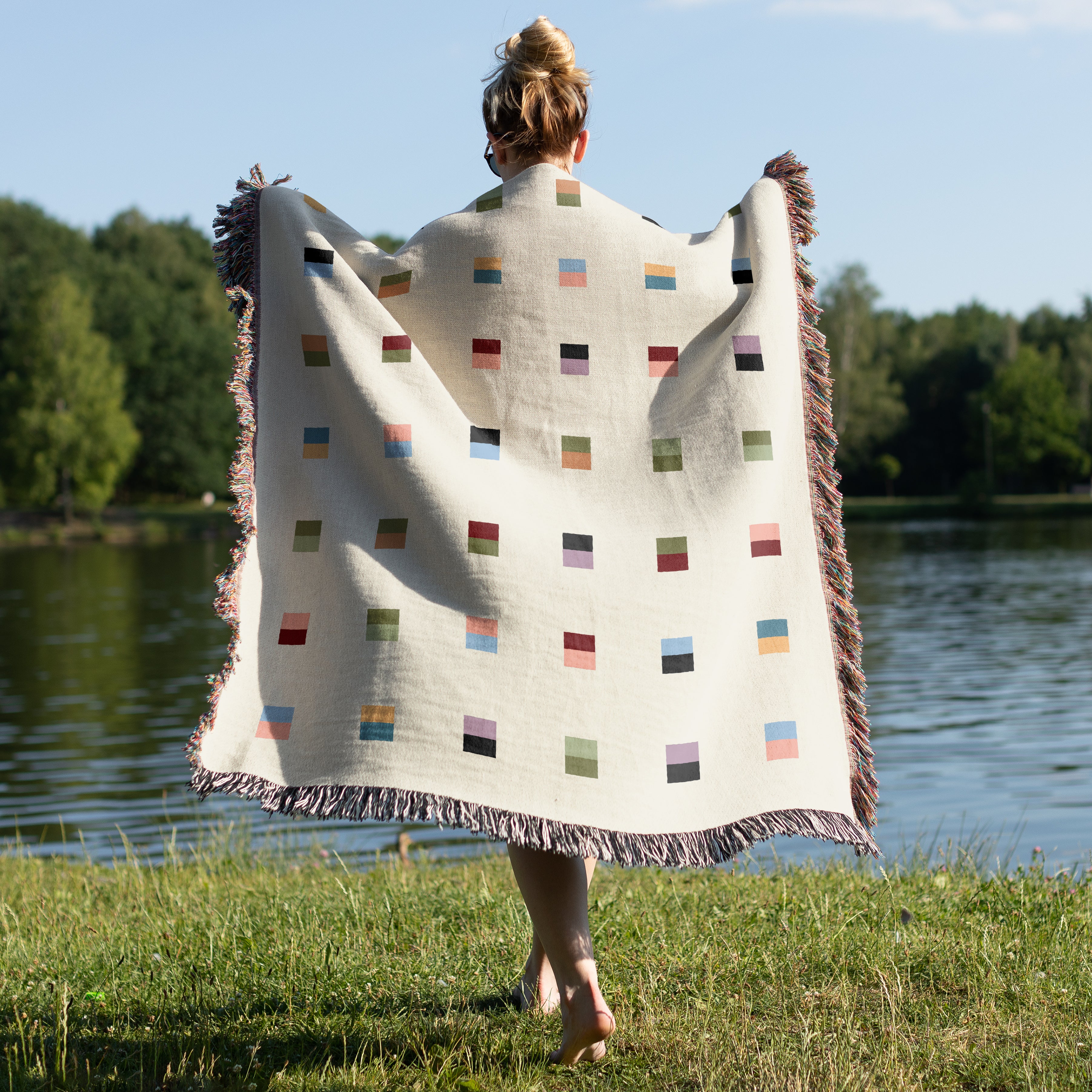 A cream-colored woven blanket with a Modern geometric split squares pattern of small multicolored squares and fringe edges. Scandinavia Design style for contemporary home decor.