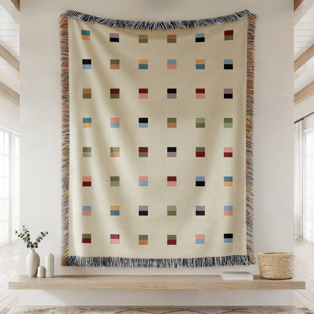 A cream-colored woven blanket with a Modern geometric split squares pattern of small multicolored squares and fringe edges. Scandinavia Design style for contemporary home decor.